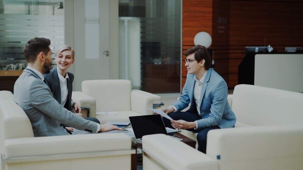 three-professionals-in-a-modern-office-lounge-njiehsp0y5u Cheerful businessman discussing financial reports with business partners sitting on sofa in modern office hall indoors